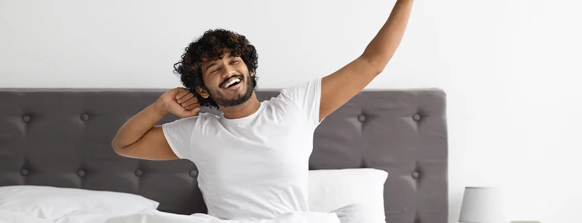 A man waking up in the morning and stretching in bed